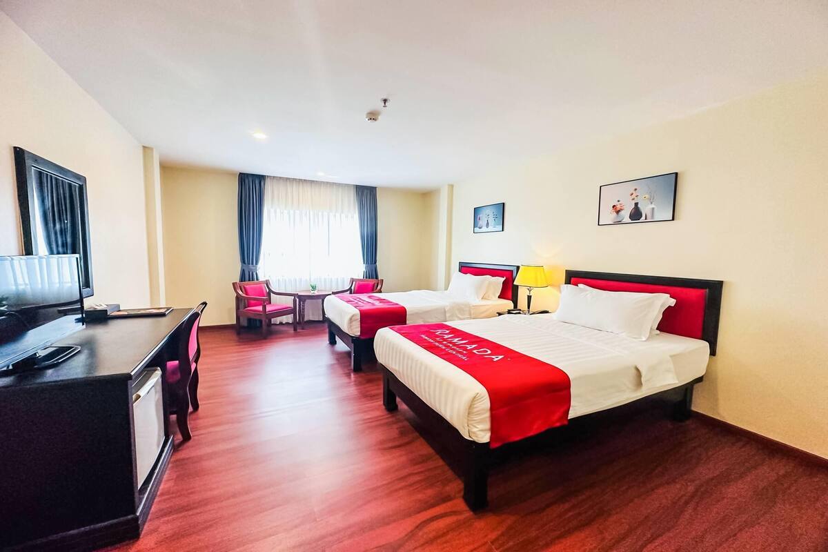Une chambre d’hôtel avec deux lits, un bureau, une chaise, une télévision et une fenêtre avec des rideaux.