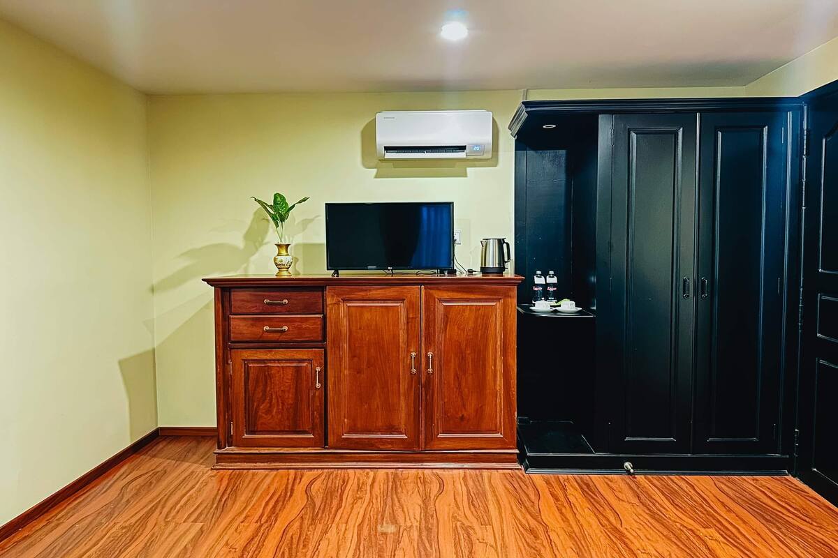 Une chambre avec un meuble en bois, un téléviseur à écran plat, un climatiseur et une armoire noire.