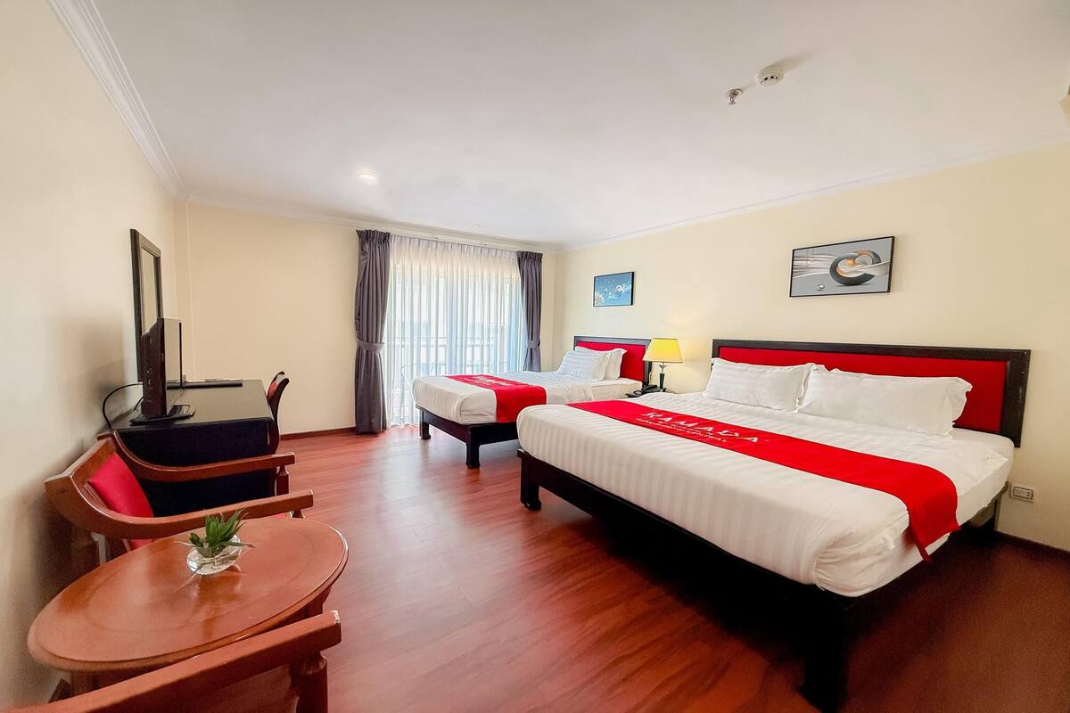 Une chambre d’hôtel avec deux lits, un bureau, une chaise, une télévision et une fenêtre avec des rideaux.