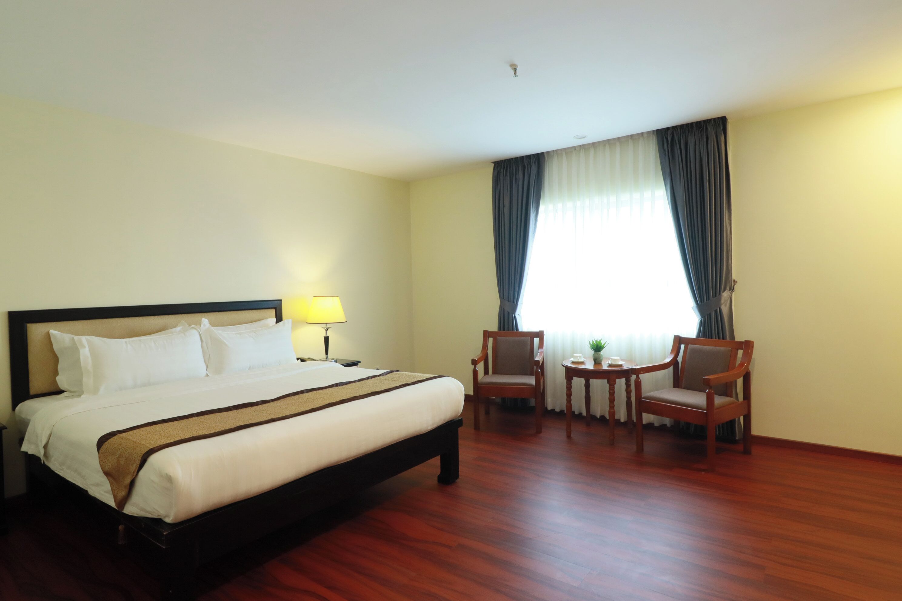 A hotel room with a large bed, two chairs, a small table, and a lamp.