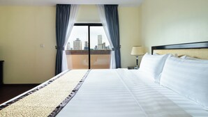 Une chambre d’hôtel avec un grand lit, une vue sur la ville par la fenêtre et une table de chevet avec une lampe.