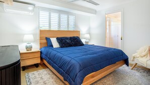 Un dormitorio con cama, mesitas de noche, ventilador de techo y ventana con persianas.