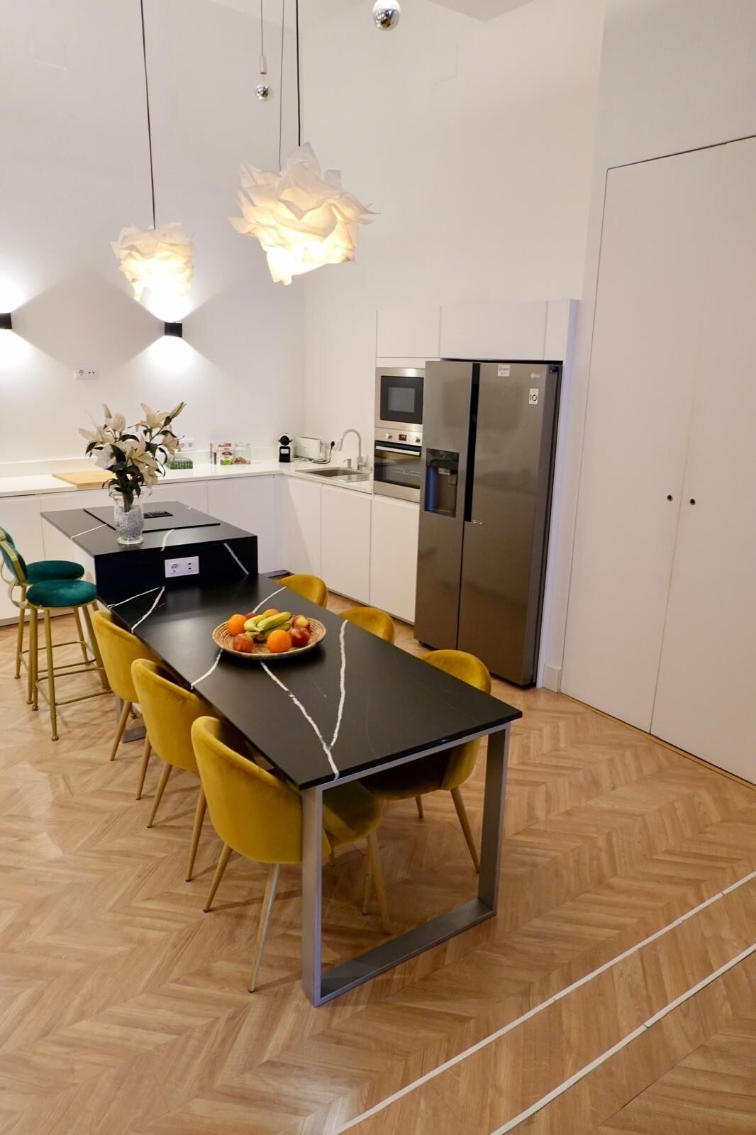 A modern kitchen with a dining area, featuring a black table, yellow chairs, a refrigerator, and a microwave.