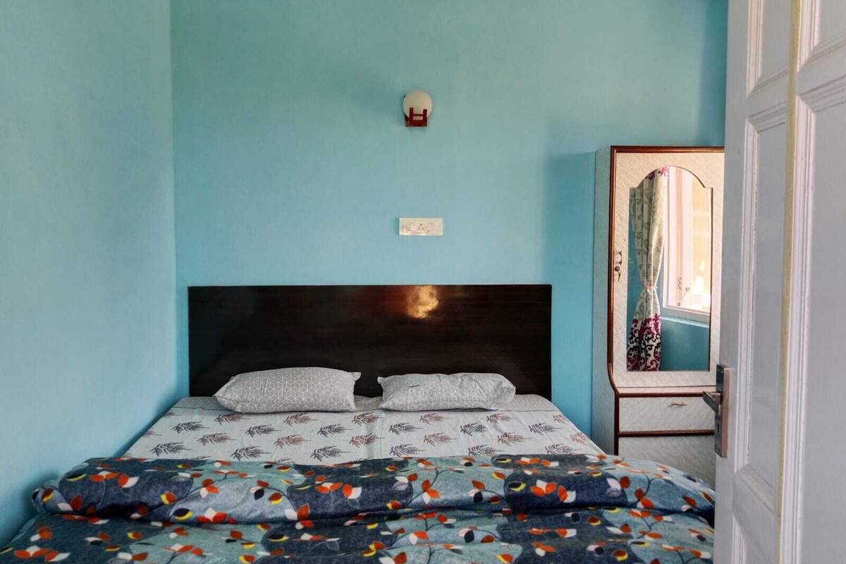 A bedroom with a bed, a nightstand, a mirror, and a wall socket.