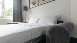 Relax in a serene space with a neatly made bed and a comfortable armchair, offering a view of the outdoors.