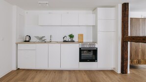 Een kleine keuken met witte kastjes, een houten aanrechtblad, een inbouwoven en een rustieke houten deur.