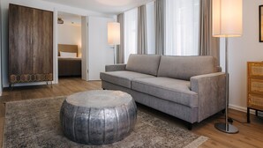 Een moderne woonkamer met een grijze bank, een rond poef en een houten garderobe.