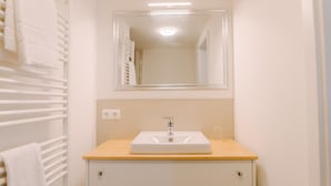 Een badkamer met een witte wastafel, een spiegel erboven en een handdoekrek met handdoeken.
