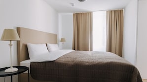 Een hotelkamer met een bed, twee bedlampen, een raam met gordijnen en een klein tafeltje.