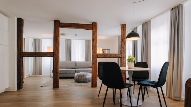 Een moderne woonkamer met een houten balkenplafond, een grijze bank en een eethoek met twee zwarte stoelen en een tafel.
