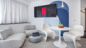 A modern living room with a flat-screen TV, white furniture, and a fruit bowl on a small table. - zzzpace Smart-Hotel Krefeld (Krefeld)