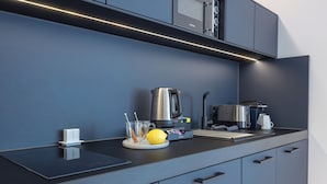A modern kitchen with a black countertop, stainless steel appliances, and a blue wall. - zzzpace Smart-Hotel Krefeld (Krefeld)