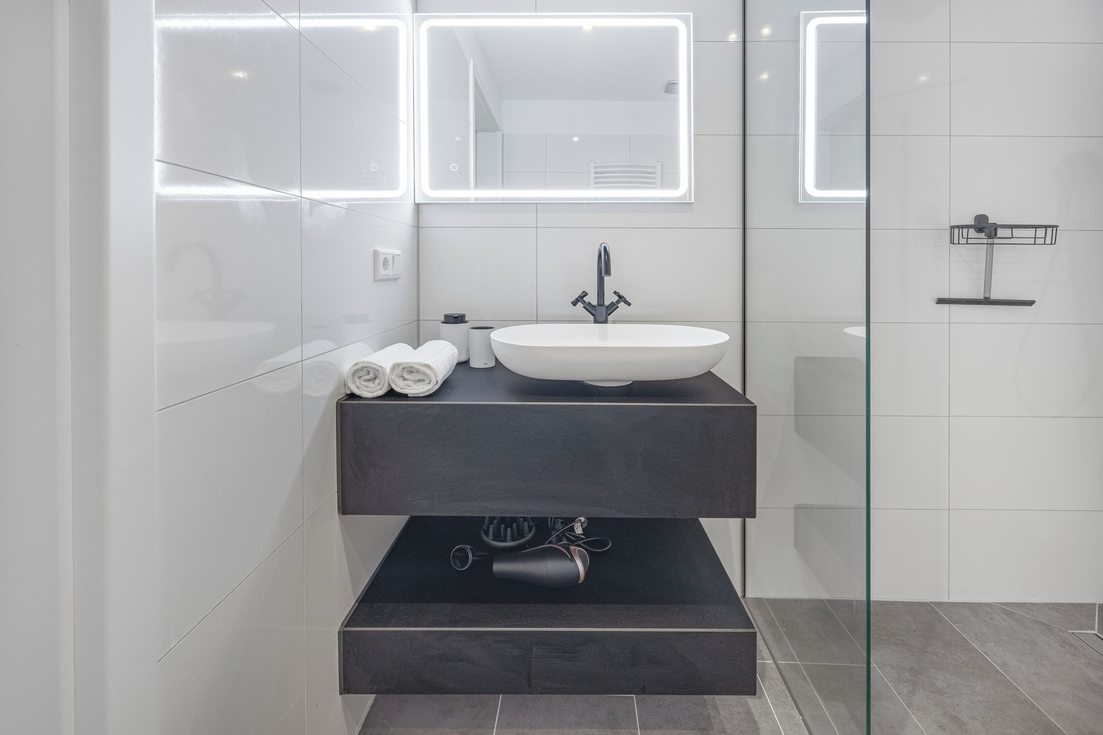 A modern bathroom with a white sink, dark countertop, and a glass shower enclosure.