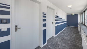 A hallway with white and blue walls, a carpeted floor, and a door marked with the number 6. - zzzpace Smart-Hotel Krefeld (Krefeld)