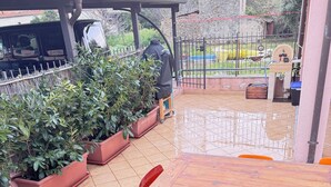 Eine Terrasse mit Holztisch und orangefarbenen Stühlen, umgeben von Blumentöpfen und einer Steinmauer.