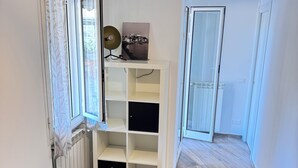 Ein Zimmer mit einem Bett, einem weißen Regal, einem Heizkörper und einem fenster mit Vorhängen.