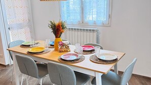 Ein Essbereich mit einem Holztisch, gedeckt für vier Personen, grauen Stühlen, einer gelben Vase mit Trockenblumen und einer hängenden Pendelleuchte.