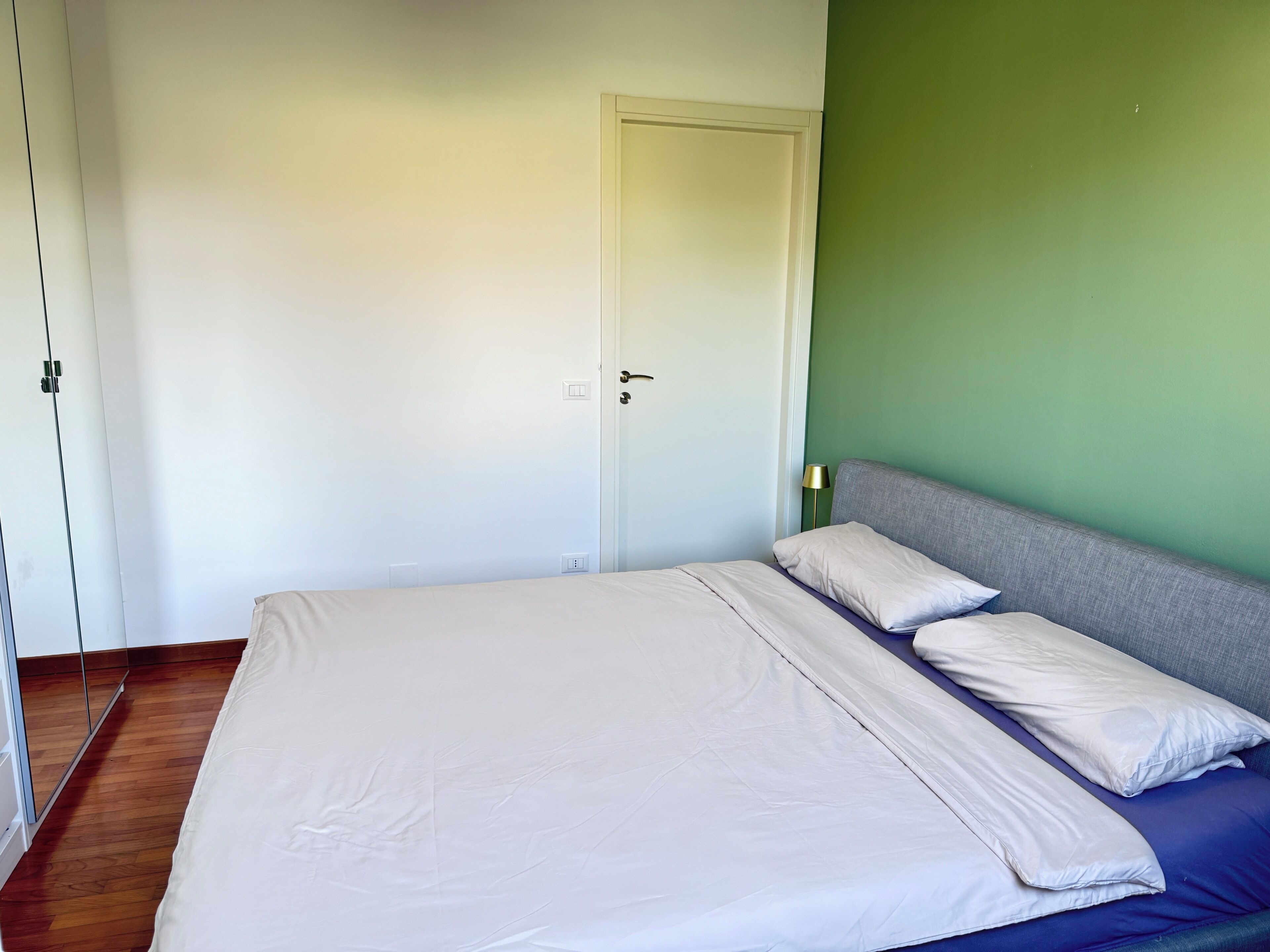 A bedroom with a bed, a door, and a green wall.