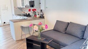 Ein modernes Wohnzimmer mit einem grauen Sofa, einem Holztisch mit Blumenvase und einer Küche im Hintergrund.