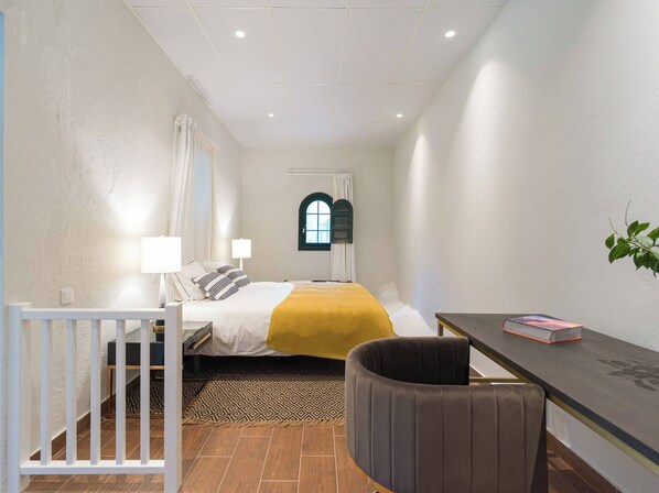 A bedroom with a bed, bedside tables, a desk, a chair, a window, and a plant. - Loft África Villas Cruz Mayor (Telde)