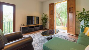 A living room with a flat-screen TV, leather sofas, a glass coffee table, and a view of greenery through a sliding glass door. - Loft África Villas Cruz Mayor (Telde)