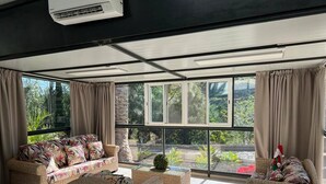Ein geräumiges Wohnzimmer mit Rattanmöbeln, großen Fenstern und einer Klimaanlage.