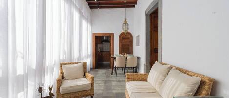 Un corredor amplio con mobiliario de mimbre, una mesa de vidrio y un comedor con puerta de madera y candelabro.