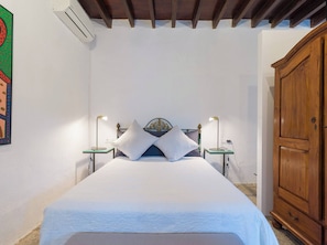 Une chambre à coucher comprenant un lit, deux tables de chevet, une armoire et un appareil de climatisation.