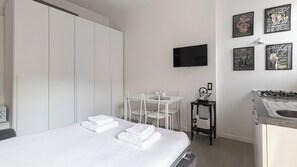 Een hotelkamer met een bed, een tafel met stoelen, een kitchenette met een fornuis en waterkoker, en een tv aan de muur.