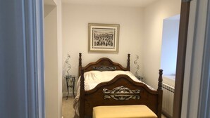Um quarto com uma cama de dossel de madeira, uma pequena mesa de cabeceira, um quadro grande na parede e uma janela com vista.
