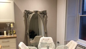 Uma sala de jantar com mesa de vidro e cadeiras brancas, um espelho grande e ornamentado e uma janela com vista.