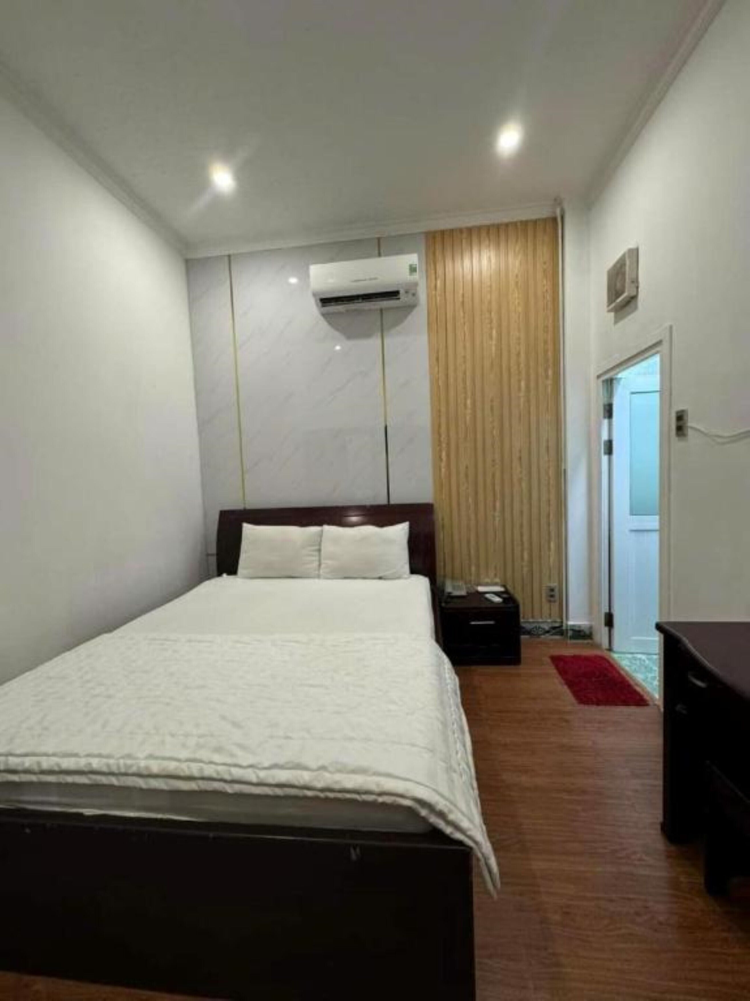 Una habitación de hotel con cama, mesita de noche, escritorio, aire acondicionado y puerta.