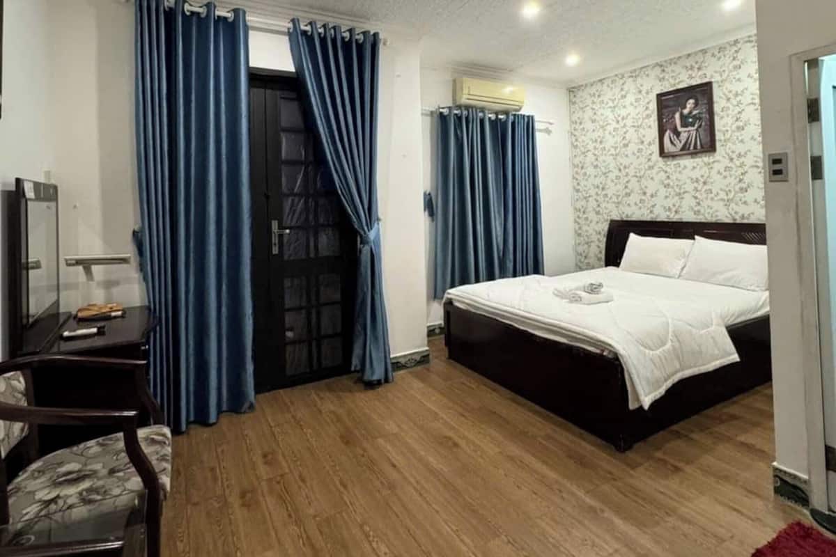 Une chambre d’hôtel avec un plancher en bois, un lit, un bureau avec une chaise et des rideaux bleus.