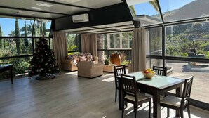 Une pièce spacieuse avec une grande fenêtre, un sapin de Noël et un coin repas comprenant une table et des chaises.