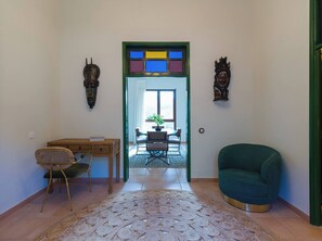 Una habitación con un escritorio, una silla y un sillón verde. Hay una pieza decorativa sobre la puerta y otra en la pared a la derecha.
