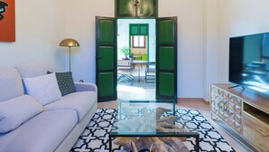 Un salon moderne avec un canapé, une table basse en verre, un téléviseur et une porte verte donnant sur un espace repas.