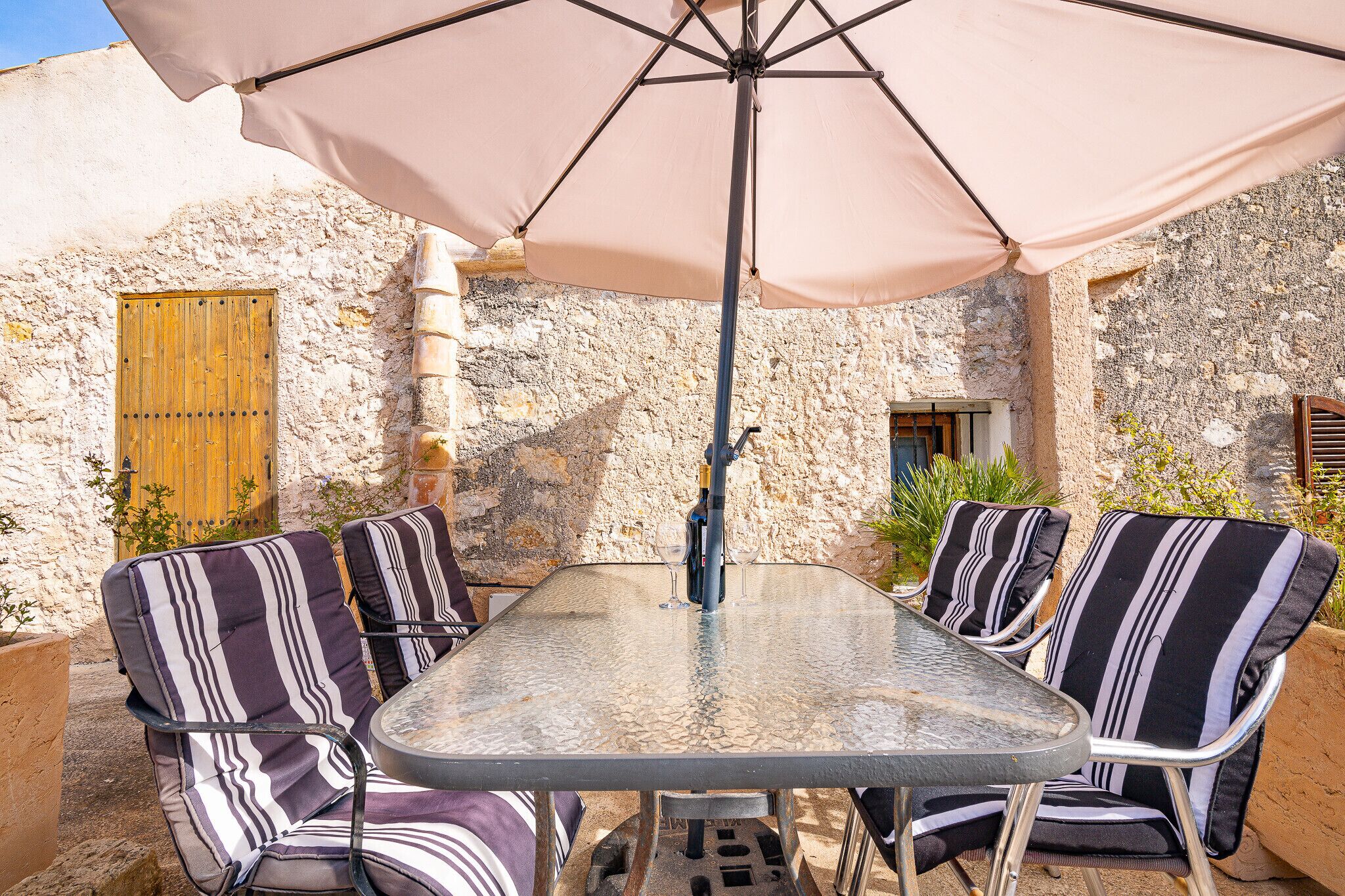 Un patio exterior con una mesa, sillas, una puerta de madera y un muro de piedra.