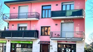 Un bâtiment rose doté de balcons, de devantures de magasins et d’une enseigne « REALE » bien visible.
