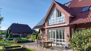 A house with a large glass window, a brick exterior, and a stone patio with outdoor furniture.