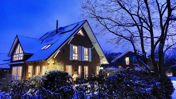 A two-story house with a steeply pitched roof, multiple windows, and a visible chimney.