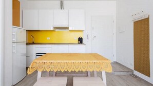 Une cuisine de taille réduite avec des meubles blancs, un plan de travail jaune et une table recouverte d’une nappe jaune.
