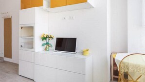 Une pièce moderne et lumineuse, aux murs blancs, avec un bureau intégré, un ordinateur portable et un vase rempli de fleurs.