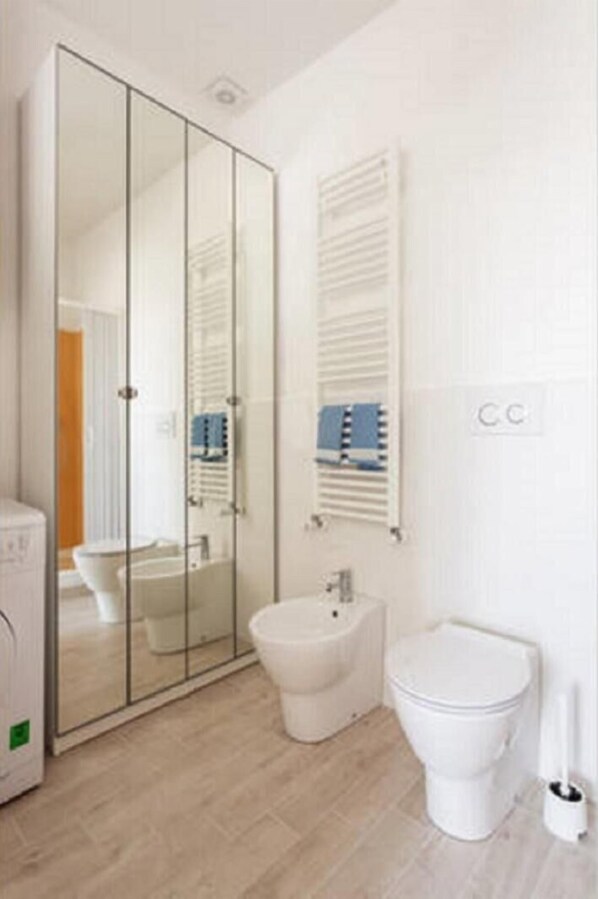 Un baño moderno con cabina de ducha de vidrio, un bidé, un inodoro y un perchero para toallas.