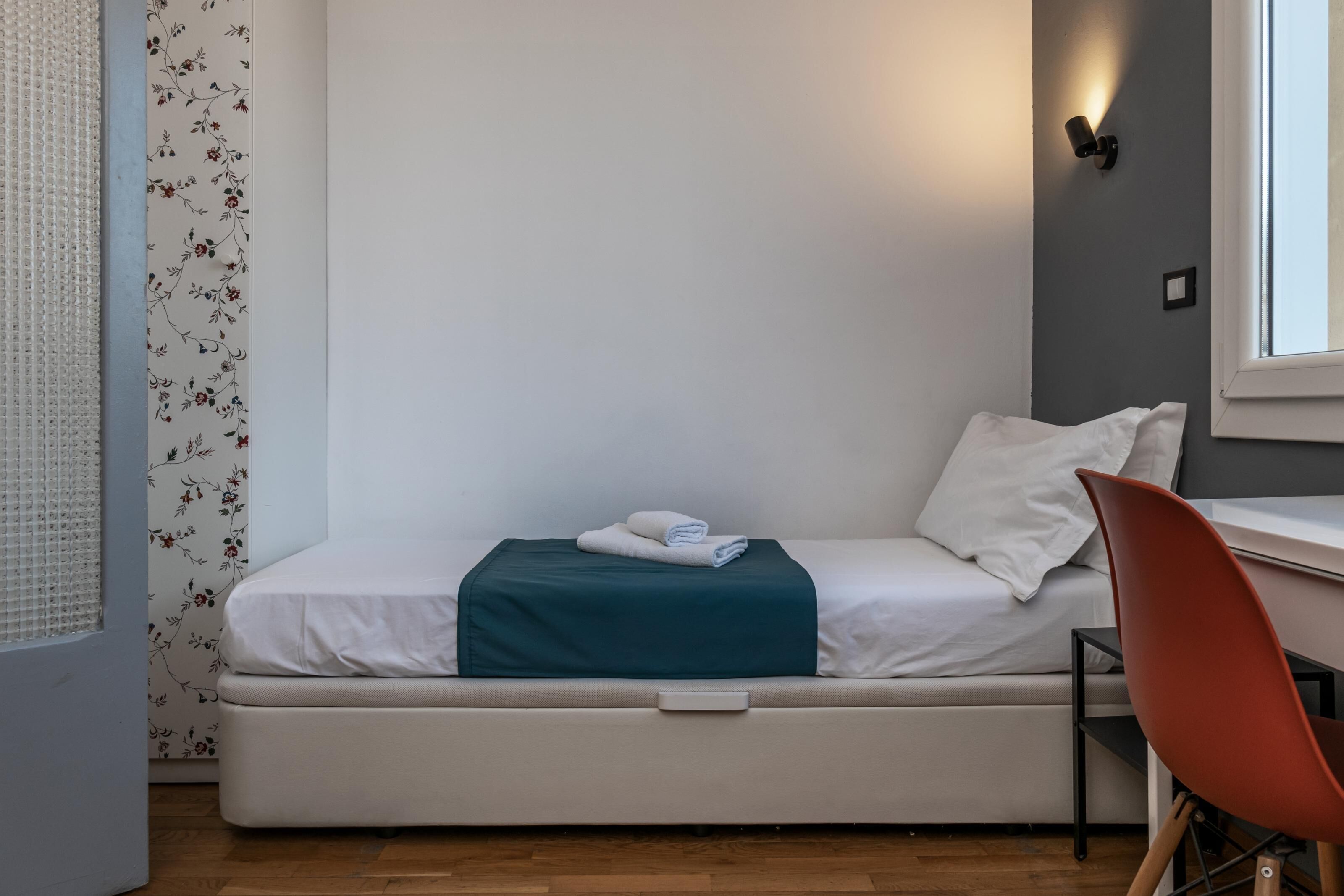 Een enkel bed met een matras, een blauwgroene deken en twee kussens in een kamer met een houten vloer.