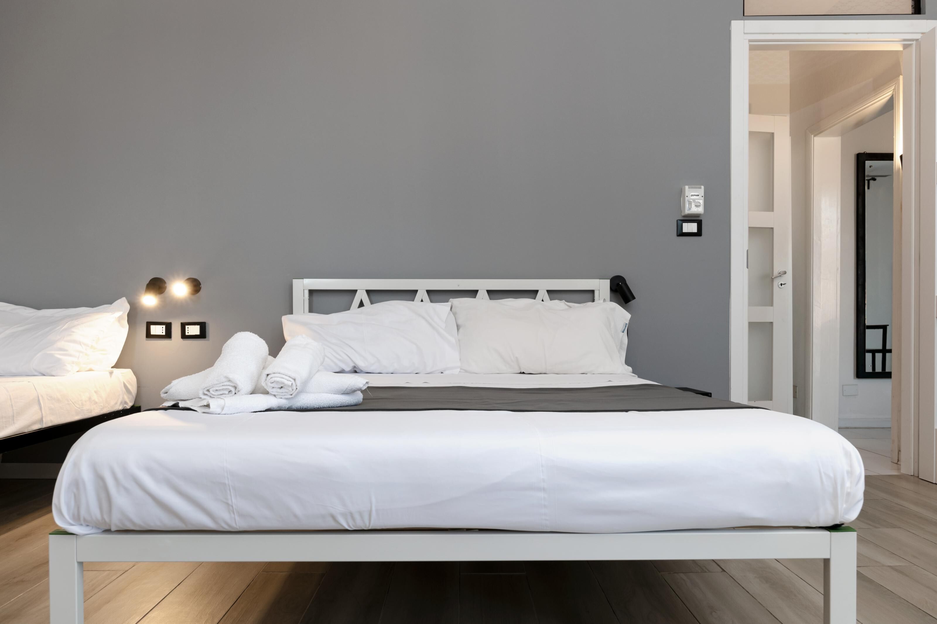 Een moderne hotelkamer met een wit bed, grijze muren en een houten vloer.