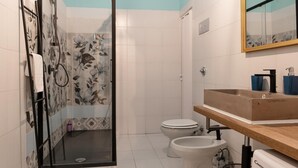 Een badkamer met douche, toilet, bidet en een wastafel met spiegel.