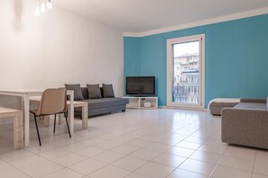 Una sala de estar moderna con un sofá gris, un televisor pequeño y un comedor con una mesa y sillas.