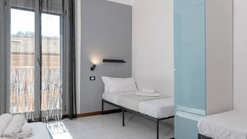 Ein modernes Hotelzimmer mit Bett, Nachttisch, Wandlampe und Blick ins Freie.