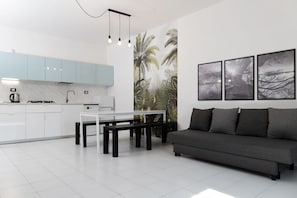 A modern kitchen with white cabinets, a dining table, and a gray sofa.