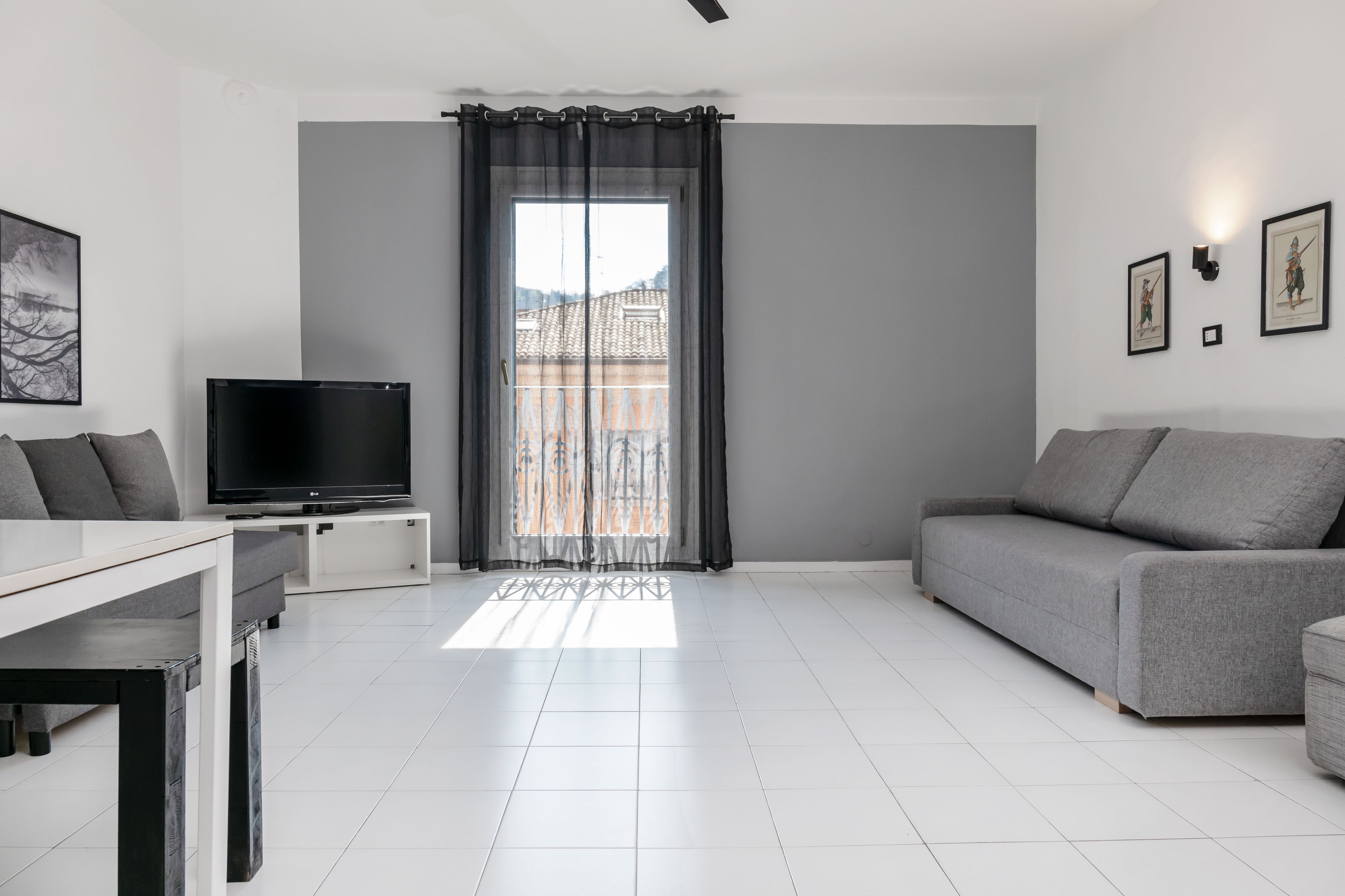 Uma sala de estar moderna com televisão de tela plana, sofá cinza e uma mesa de jantar.